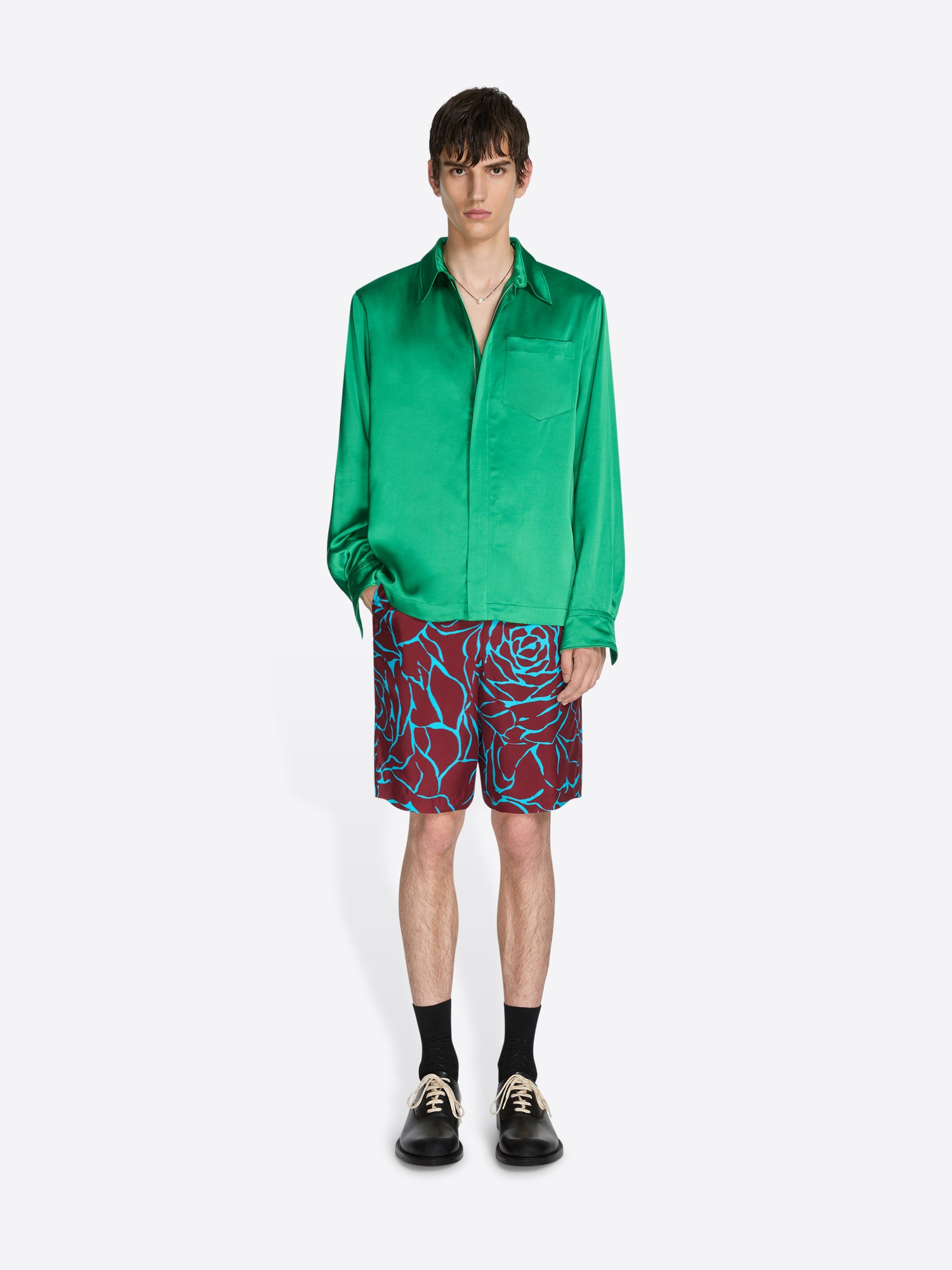 Person wearing a green satin shirt and patterned shorts on a white background - Dries Van Noten