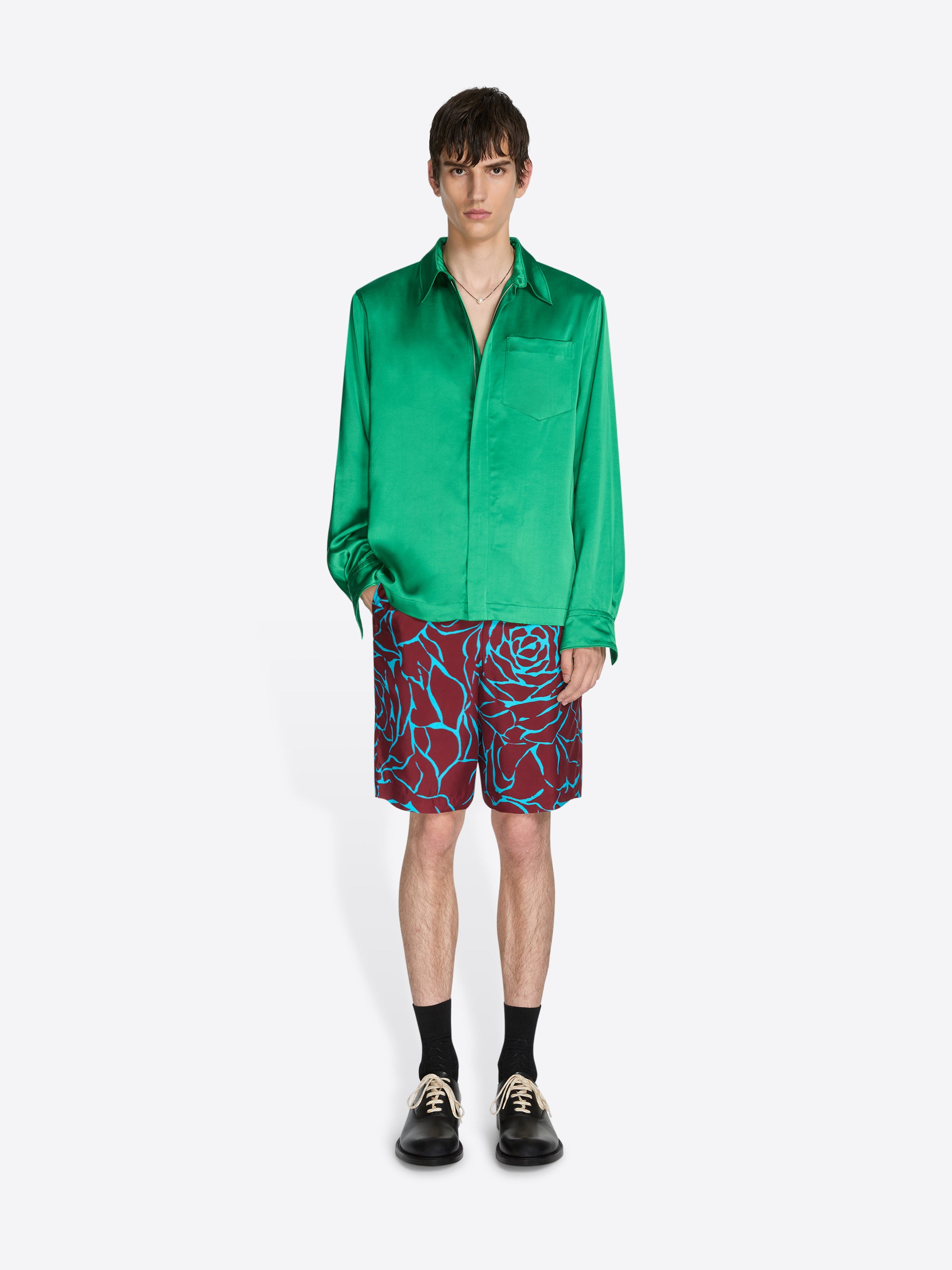 Person wearing a green satin shirt and patterned shorts on a white background - Dries Van Noten