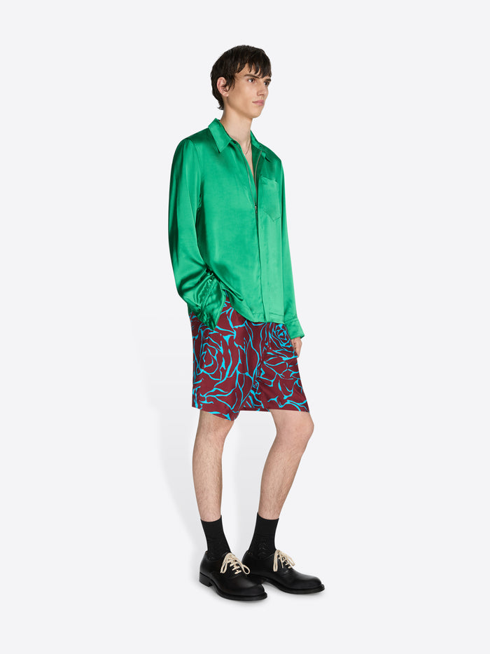 Person wearing a green satin shirt and patterned shorts on a white background