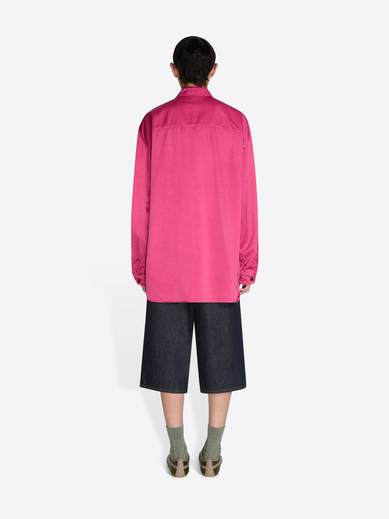 Person wearing a bright pink shirt and dark shorts on a white background - Dries Van Noten