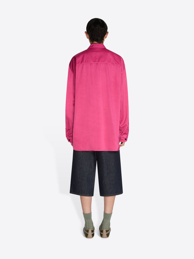 Person wearing a bright pink shirt and dark shorts on a white background - Dries Van Noten