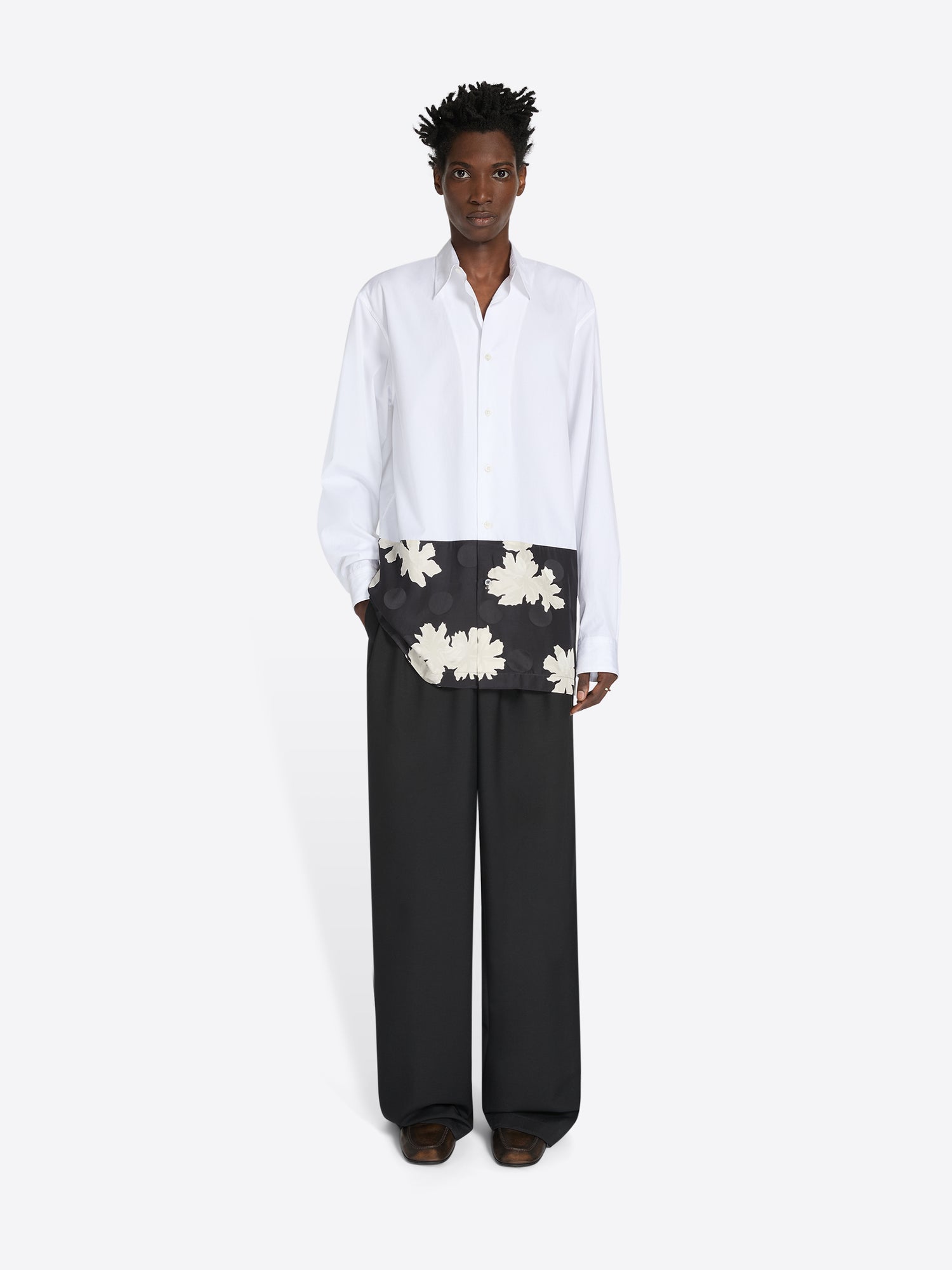 Person wearing a white shirt and black pants with floral patterns on a white background