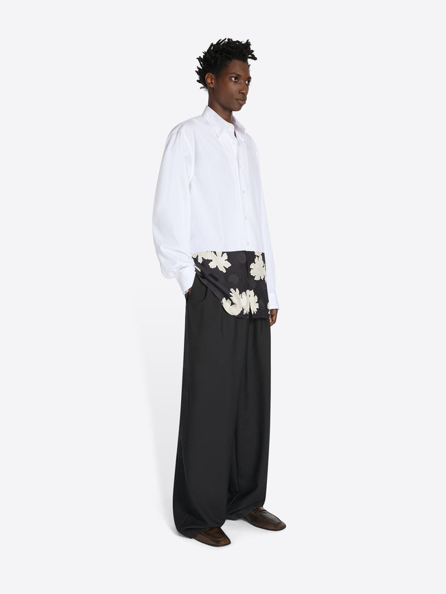 Person wearing a white shirt and black pants with floral patterns on a white background