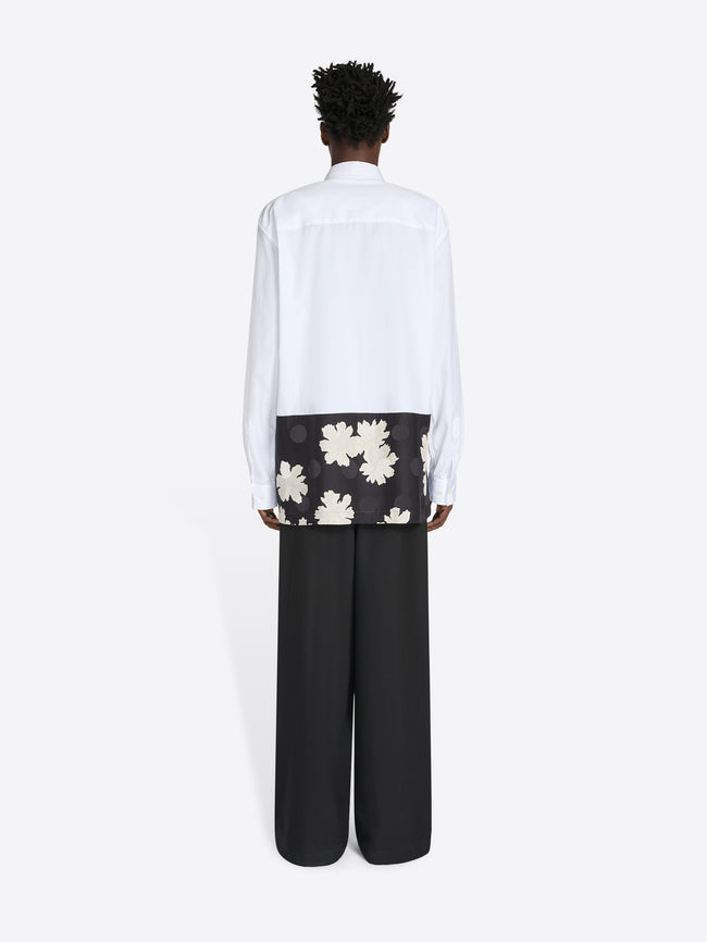 Person wearing a white shirt with floral design and black pants on a white background