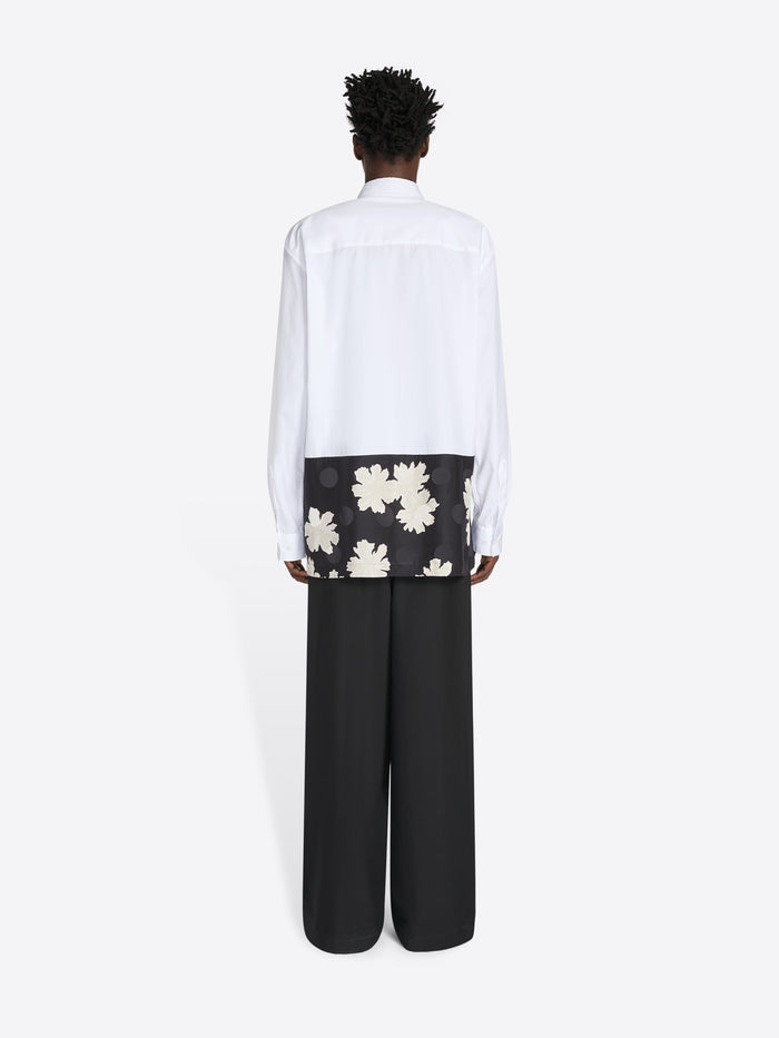 Person wearing a white shirt with floral design and black pants on a white background