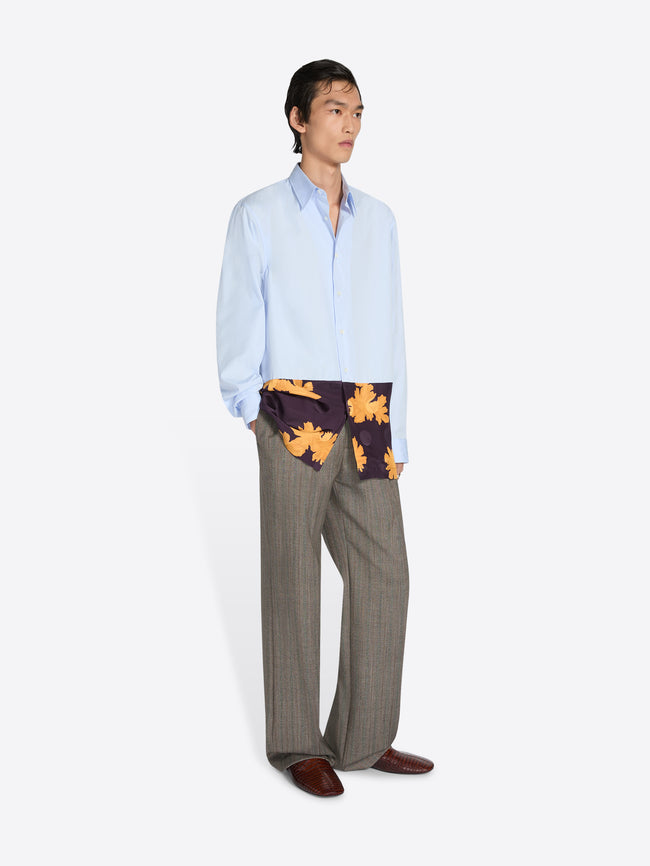 Person wearing a light blue shirt, patterned end, and gray pants on a white background