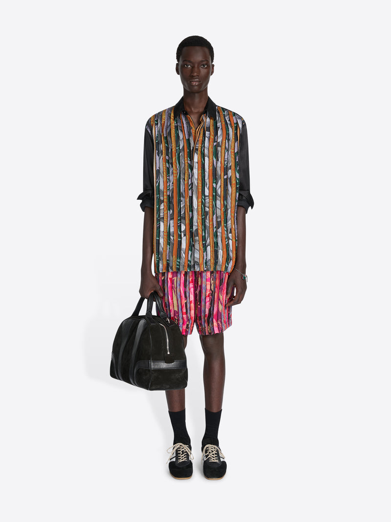 Man wearing a colorful striped shirt and shorts holding a black bag on a white background - Dries Van Noten