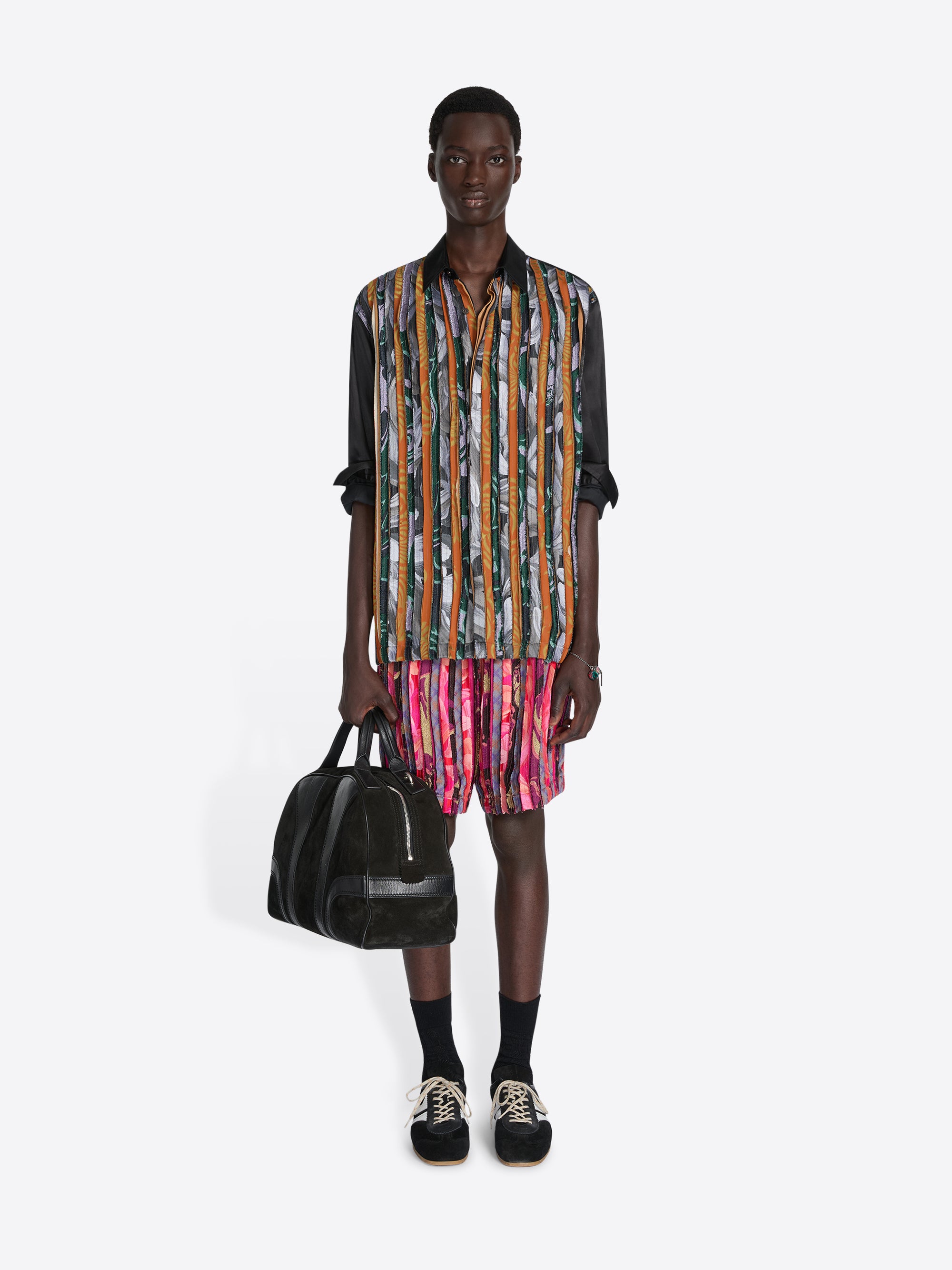Man wearing a colorful striped shirt and shorts holding a black bag on a white background - Dries Van Noten