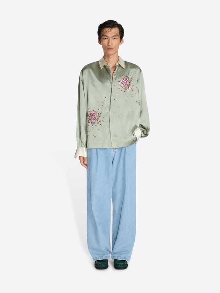 Person wearing a light green embroidered shirt and blue pants on a white background - Dries Van Noten