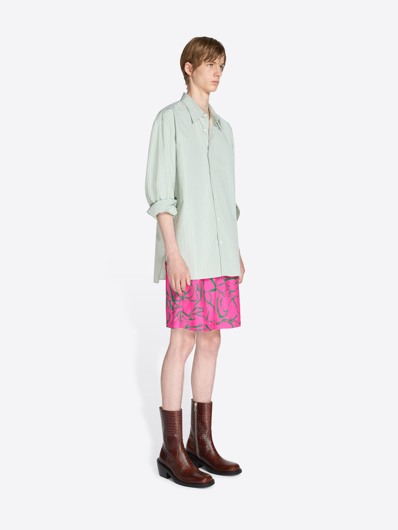 Person wearing a light green shirt, pink shorts with floral pattern, and brown boots on a white background