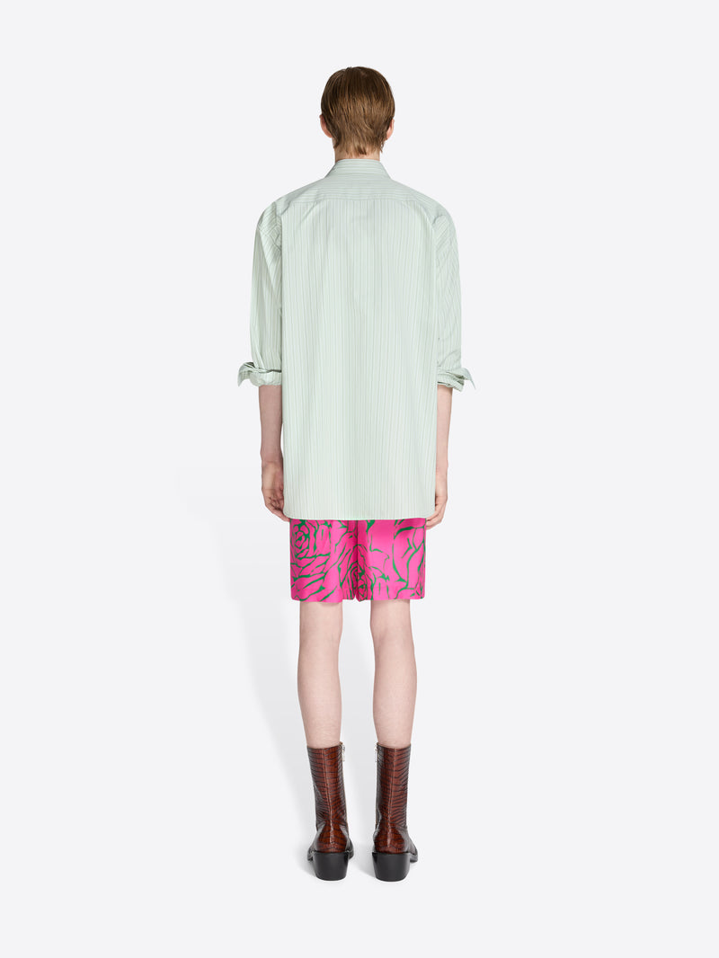 Person wearing a light green shirt and pink shorts with a white background