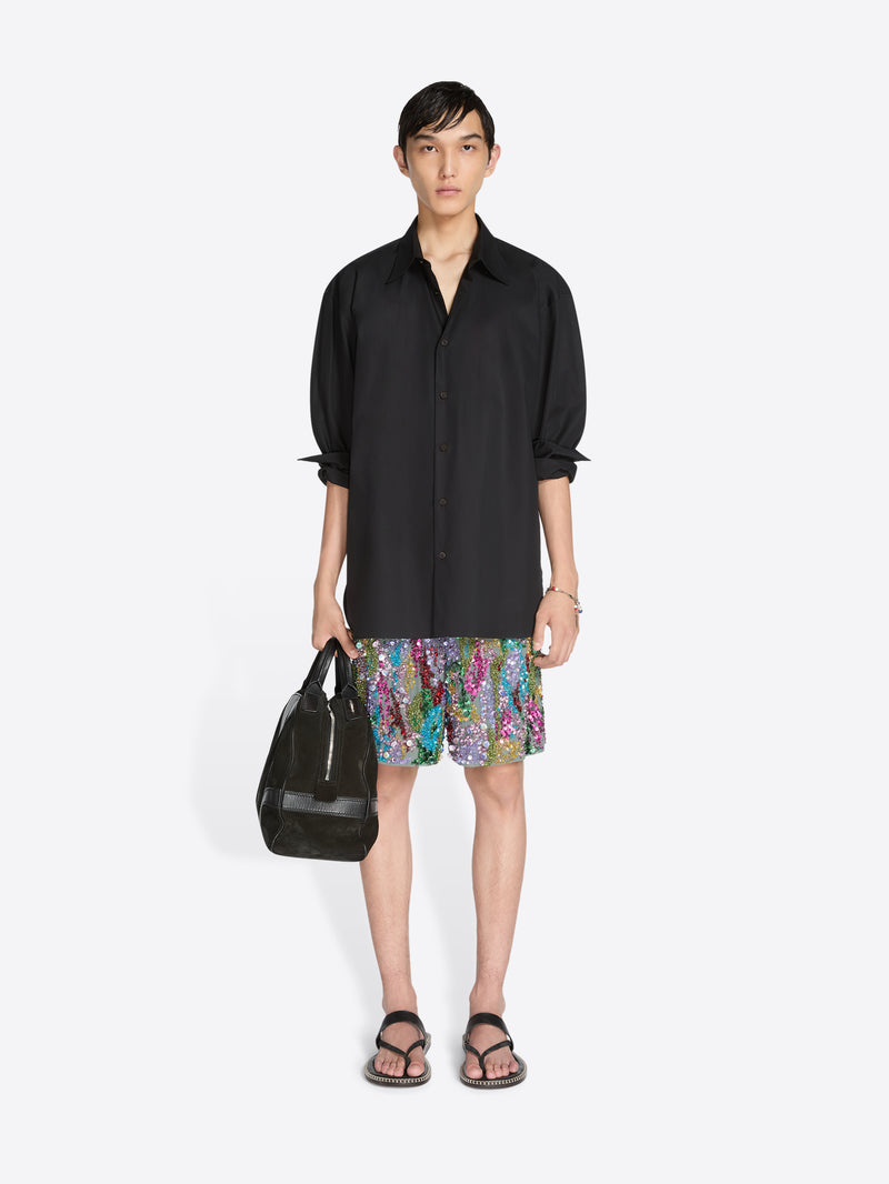 Person wearing a black shirt and colorful shorts with a black bag on a white background