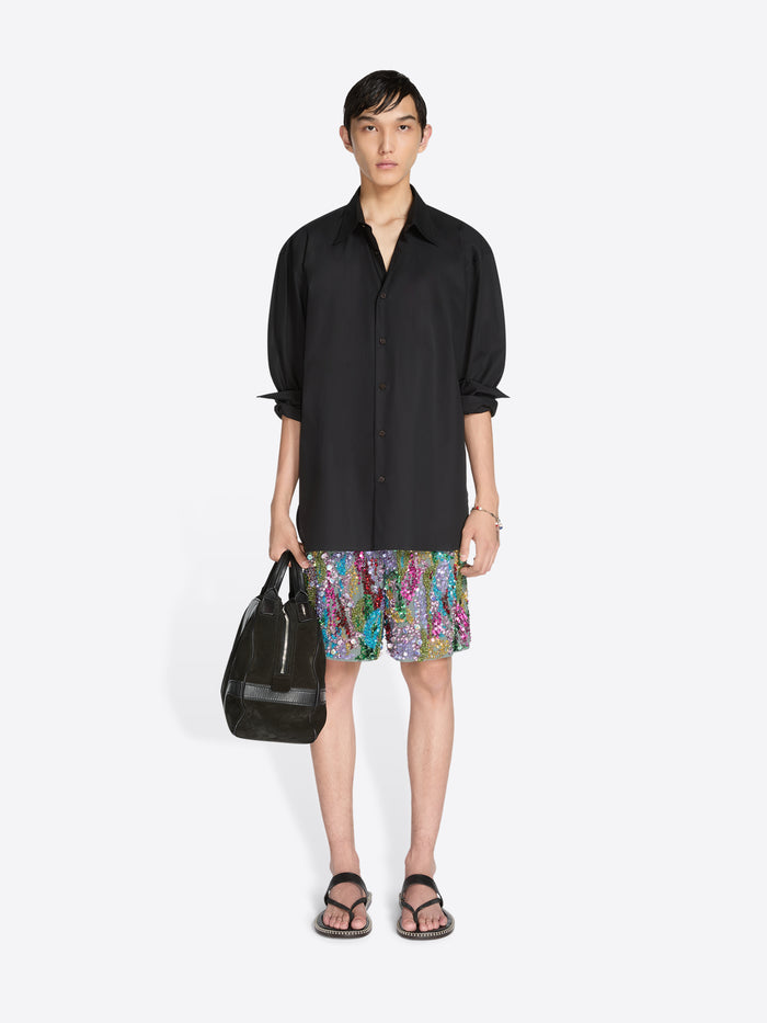 Person wearing a black shirt and colorful shorts with a black bag on a white background