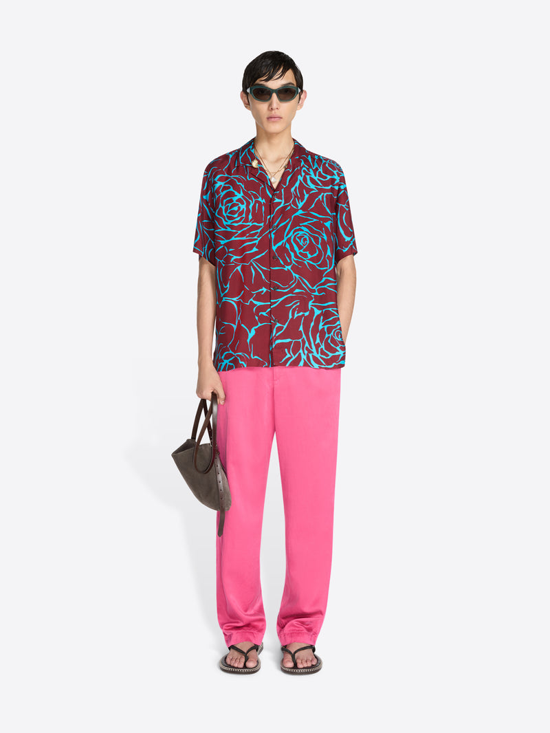 Person wearing a colorful shirt and pink pants with a handbag on a white background