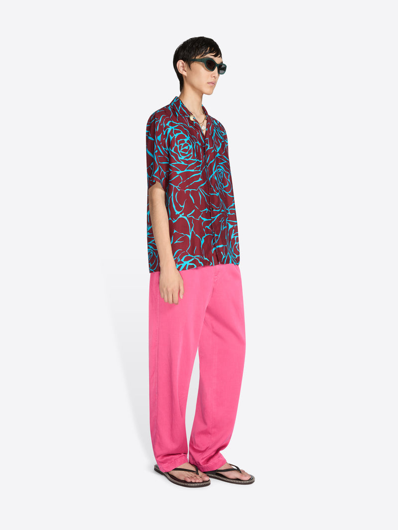 Person wearing a patterned shirt and pink pants on a white background