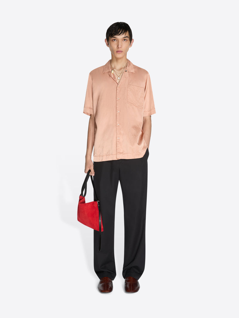 Person wearing a light pink shirt and black pants holding a red bag on a white background