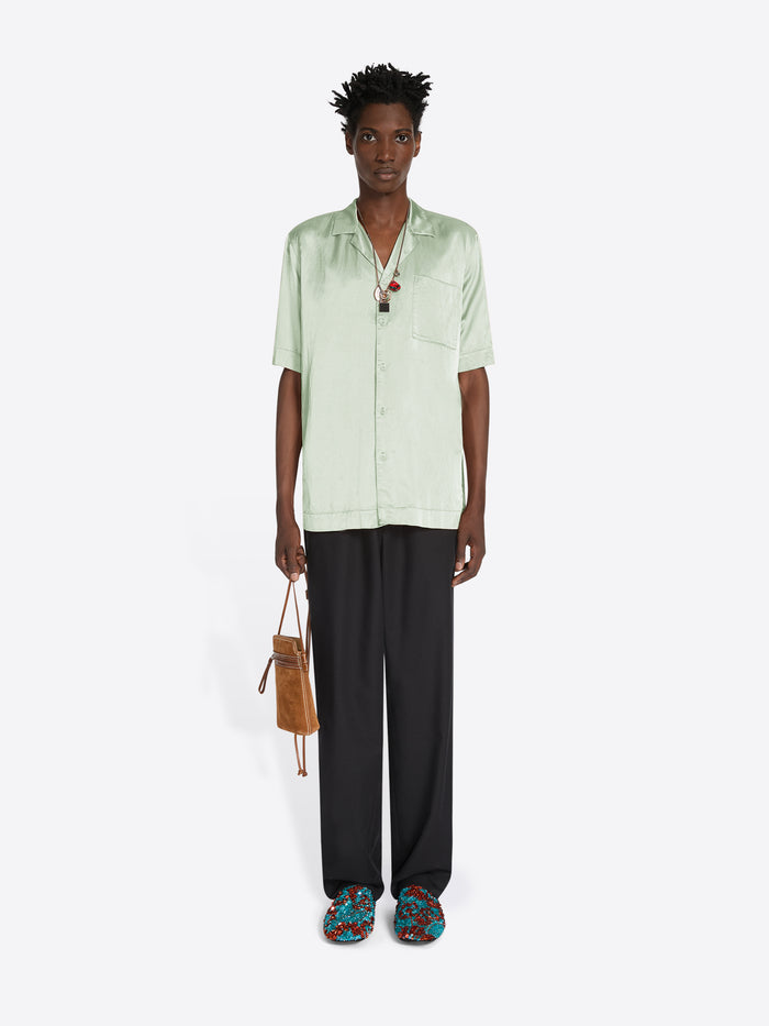 Person wearing a light green shirt and black pants with colorful shoes, holding a brown bag on a white background.