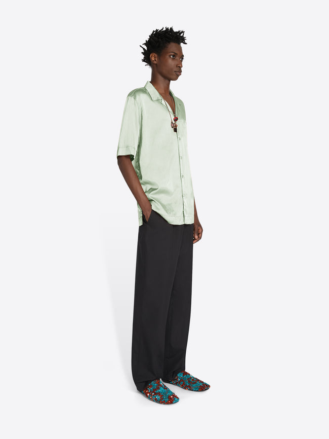 Person wearing a light green shirt and black pants on a white background