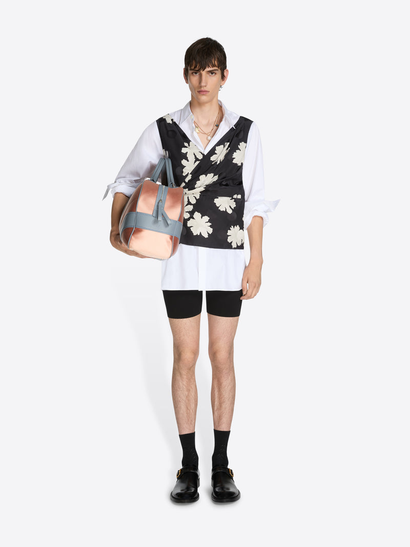 Person wearing a black floral vest over a white shirt with black shorts, holding a pink handbag on a white background.