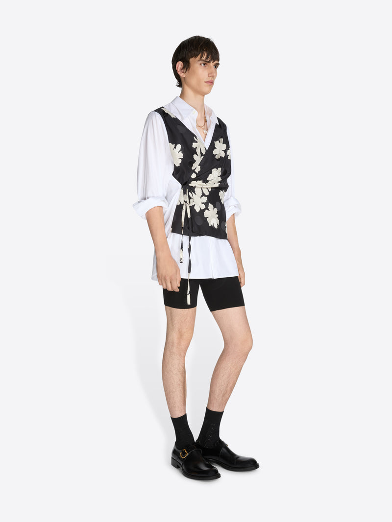 Person wearing a white shirt, black floral vest, and black shorts on a white background