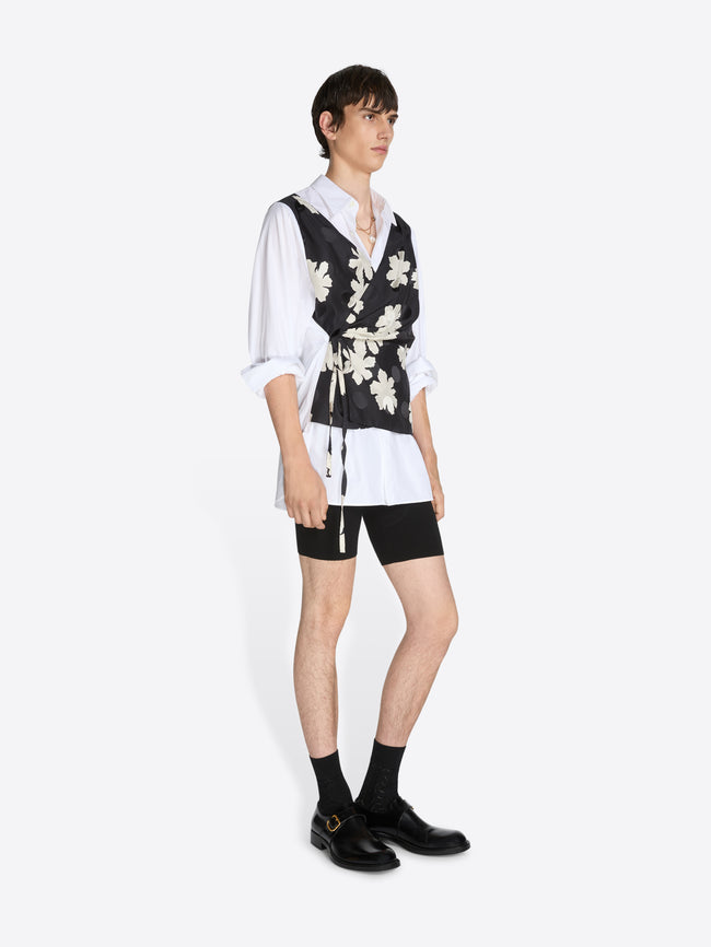 Person wearing a white shirt, black floral vest, and black shorts on a white background
