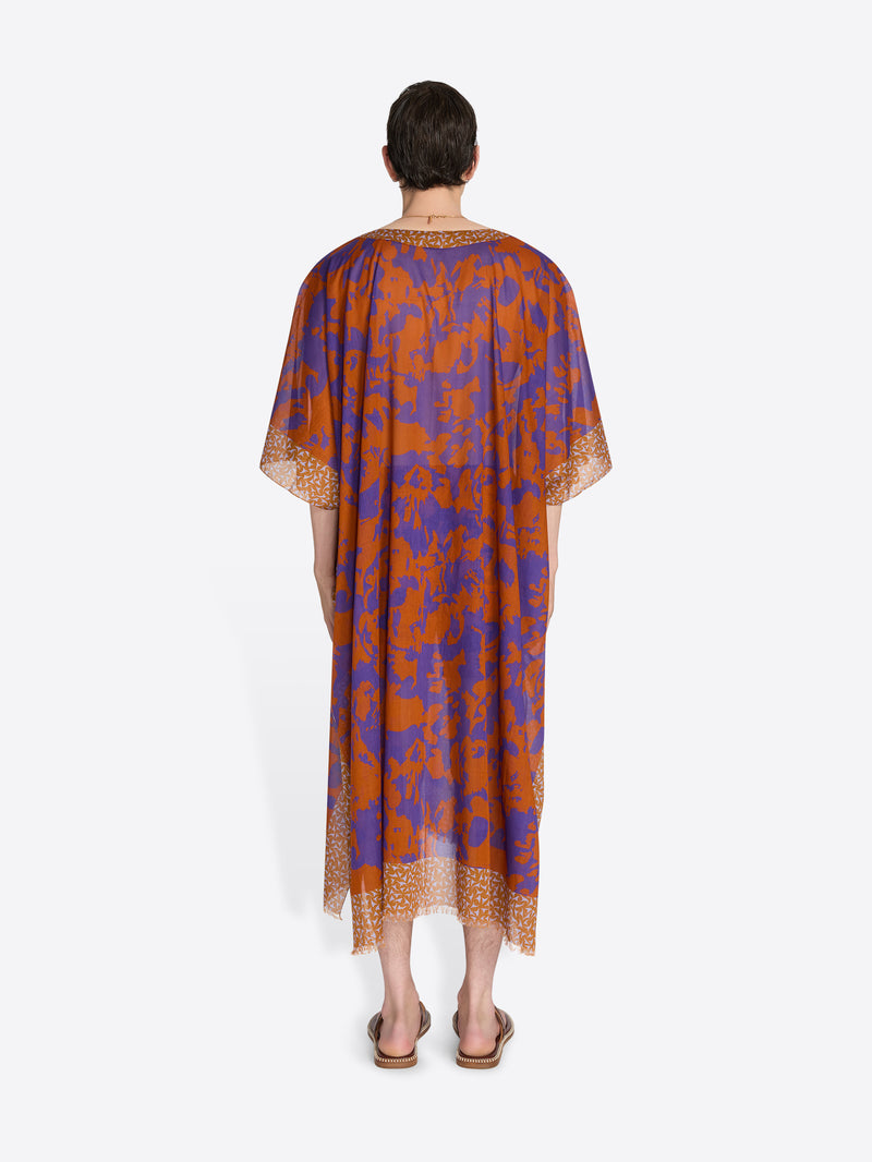 Man wearing a patterned orange and blue dress on a white background