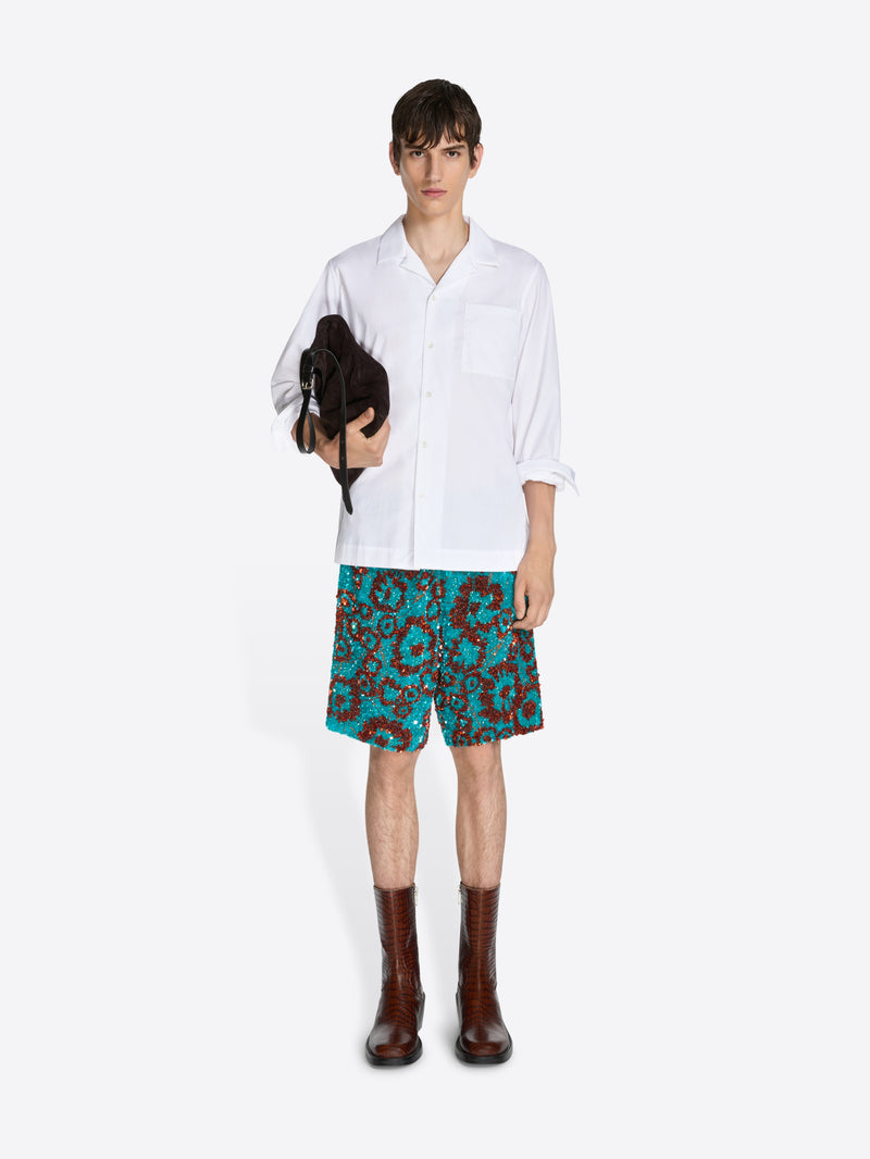 Person wearing a white shirt and patterned shorts on a white background