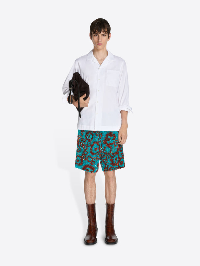 Person wearing a white shirt and patterned shorts on a white background