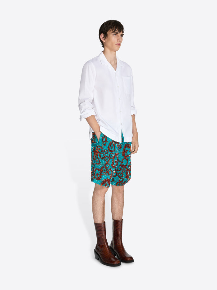 Person wearing a white shirt, teal patterned skirt, and brown boots on a white background