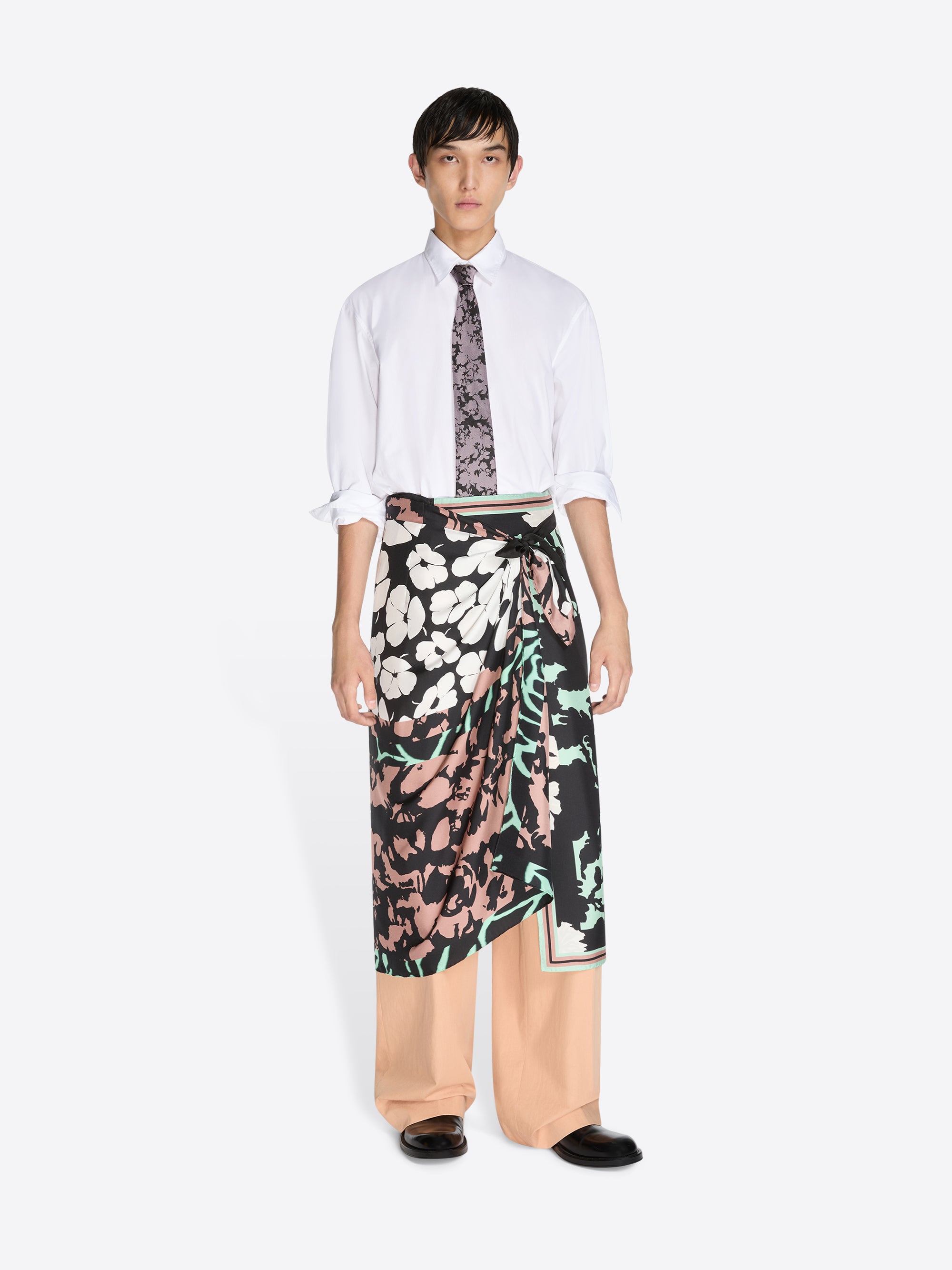 Person wearing a white shirt, patterned tie, and floral skirt on a white background - Dries Van Noten