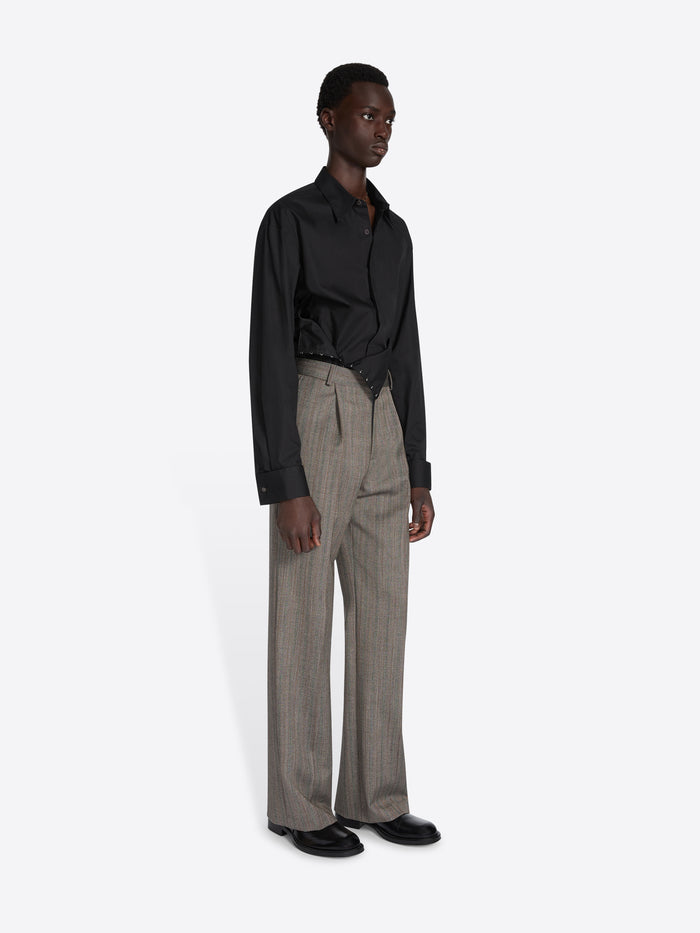 Man wearing a black shirt and gray pleated pants on a white background