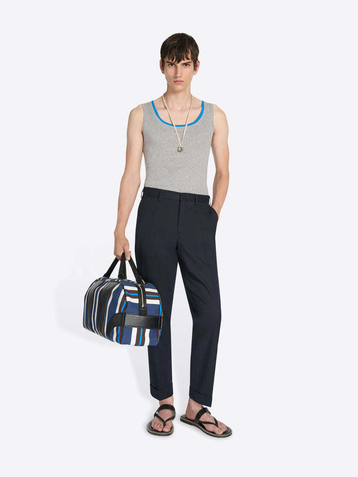 Woman holding a striped bag wearing a sleeveless top and pants on a white background