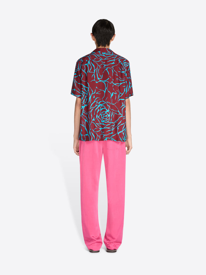 Person wearing a colorful patterned shirt and pink pants on a white background - Dries Van Noten