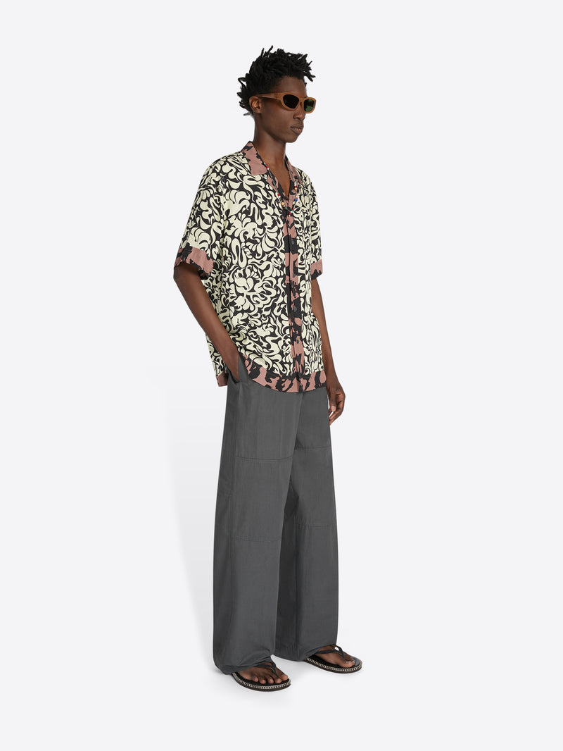 Person wearing a patterned shirt and gray pants on a white background - Dries Van Noten