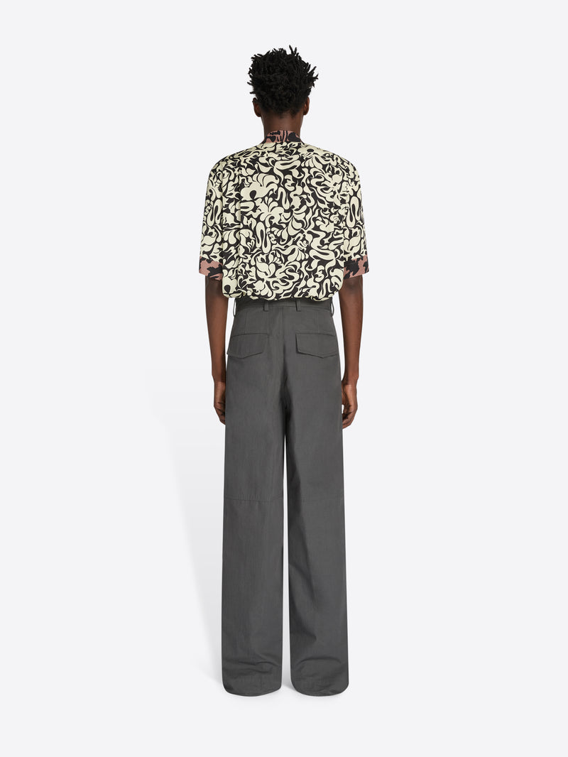 Person wearing a patterned shirt and gray pants on a white background - Dries Van Noten