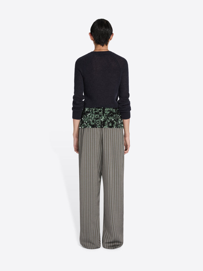 Person wearing a black sweater and striped pants with a floral hem on a white background - Dries Van Noten