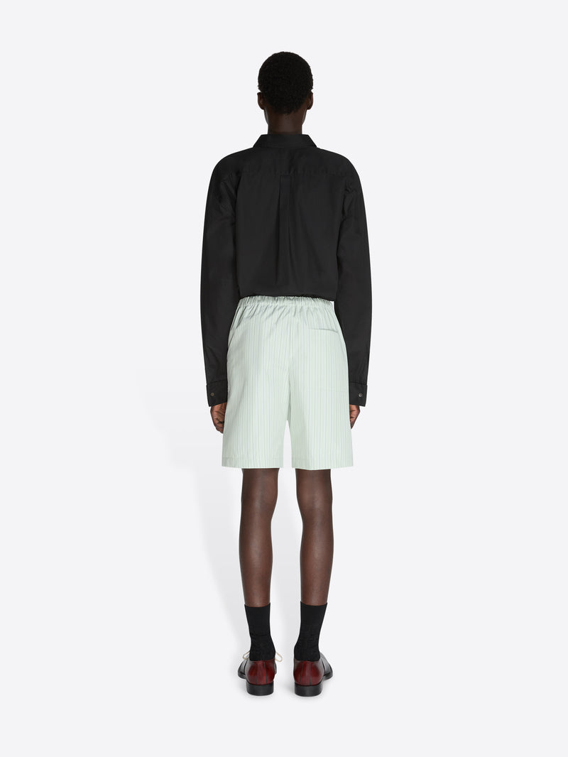 Person wearing a black jacket and light green shorts on a white background