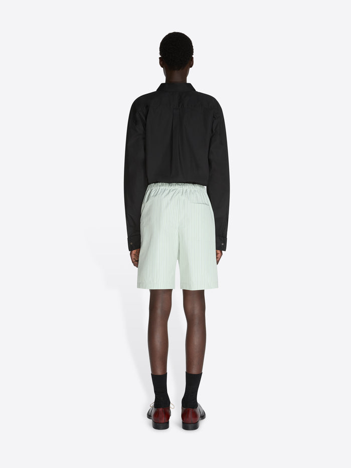 Person wearing a black jacket and light green shorts on a white background