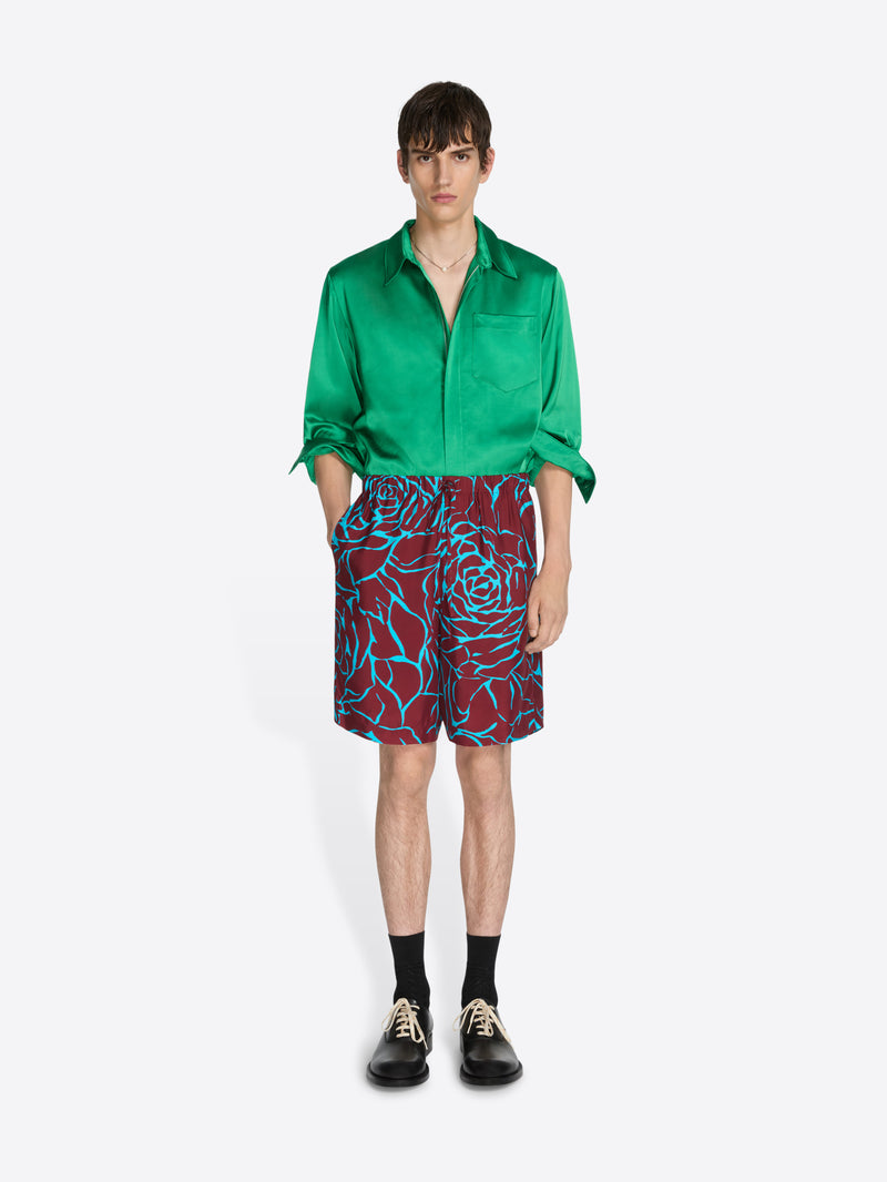 Person wearing a green shirt and patterned shorts on a white background - Dries Van Noten