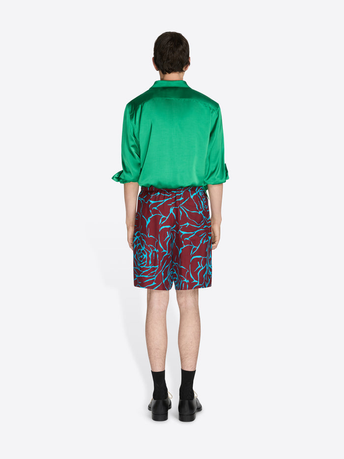 Person wearing a green shirt and patterned shorts on a white background - Dries Van Noten