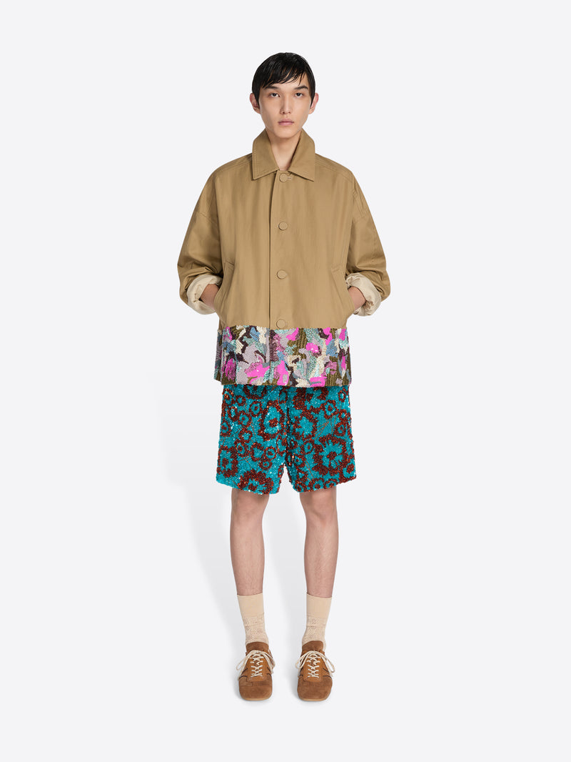 Person wearing a beige jacket, colorful shirt, and patterned shorts on a white background - Dries Van Noten