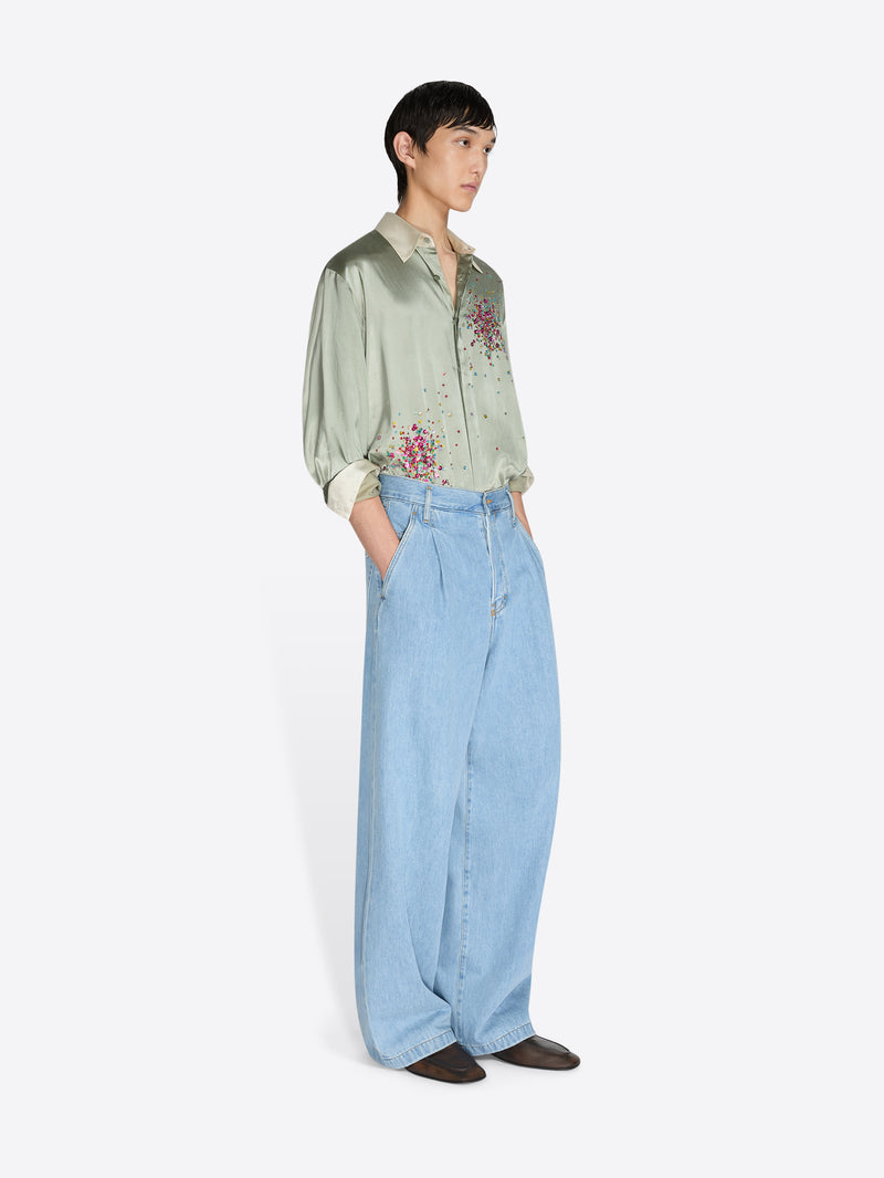 Person wearing a light green embroidered shirt and light blue jeans on a white background