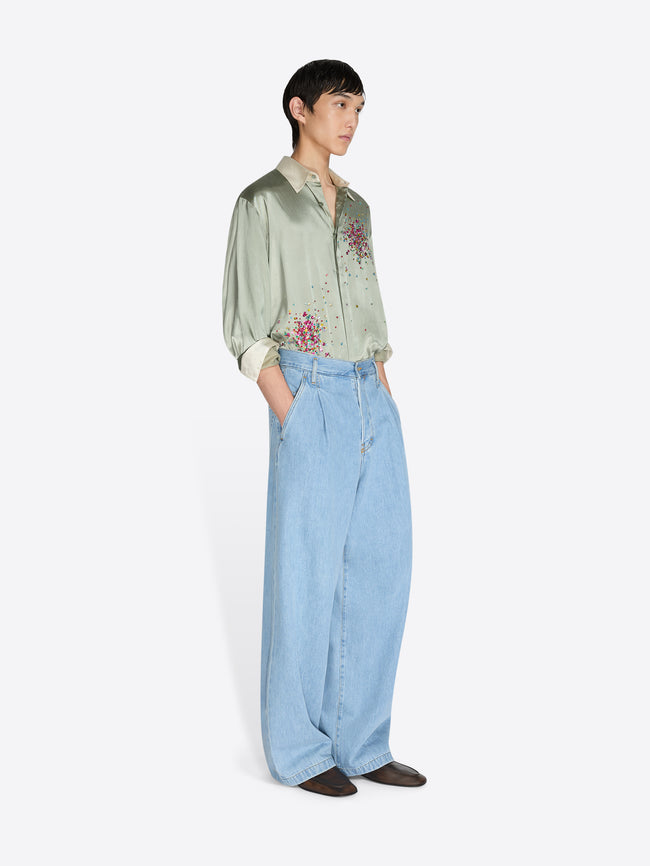 Person wearing a light green embroidered shirt and light blue jeans on a white background