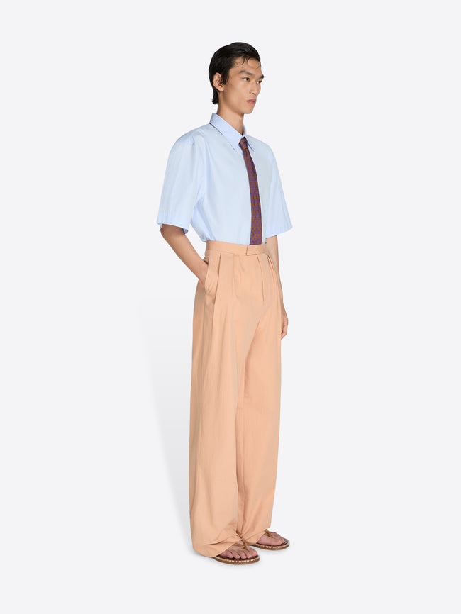 Person wearing a light blue shirt with a dark tie and beige pants on a white background - Dries Van Noten