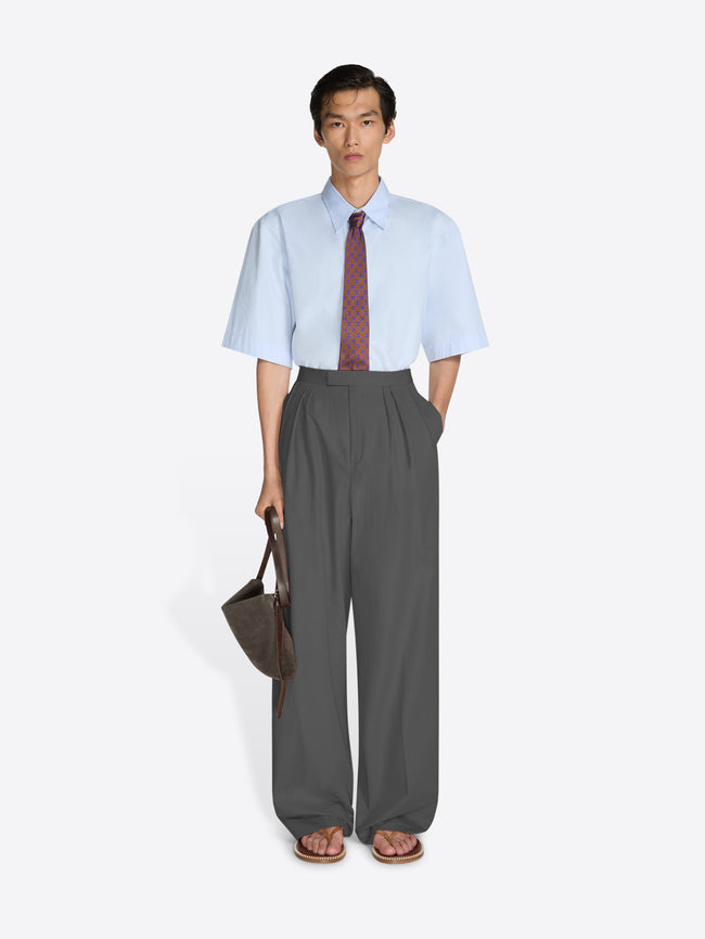 Man wearing a light blue shirt, gray pants, and a red tie on a white background - Dries Van Noten
