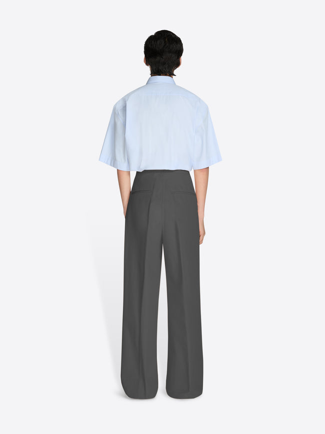Person wearing a light blue shirt and gray pants on a white background - Dries Van Noten