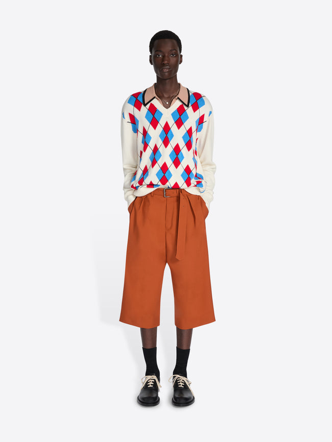 Person wearing a colorful argyle sweater and orange pants on a white background