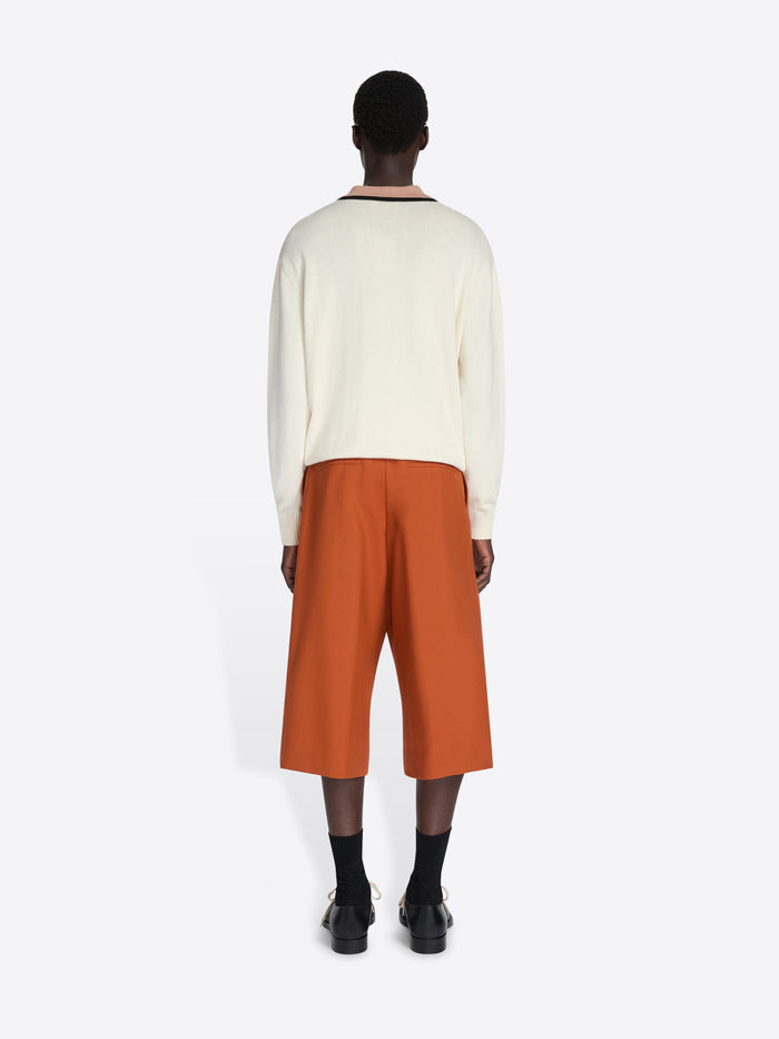 Person wearing a cream sweater and orange pants on a white background