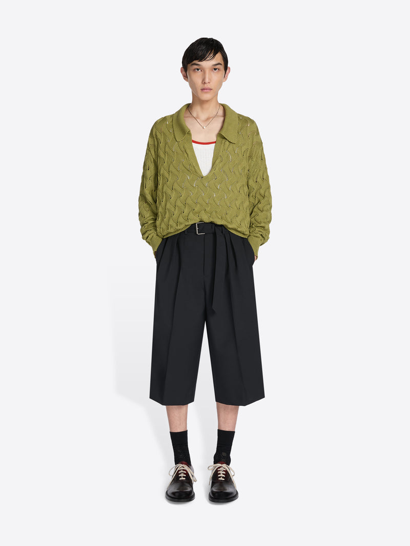 Person wearing a green textured shirt and black wide-leg pants on a white background