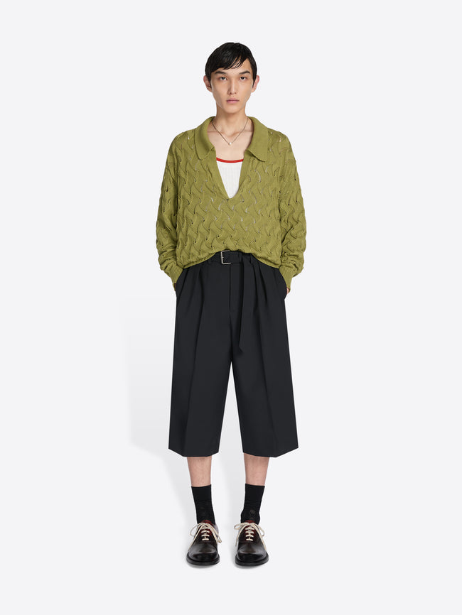 Person wearing a green textured shirt and black wide-leg pants on a white background